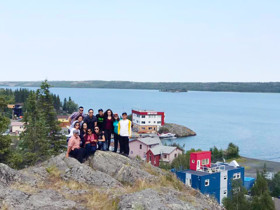 Young adult volunteers standing on top of a large rock overlooking houses and a lake